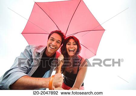 Stock Image - Couple in their 30's smiling under umbrella.. Fotosearch