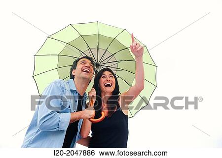 Stock Photograph - Couple in their 30's smiling under umbrella.. Fotosearch