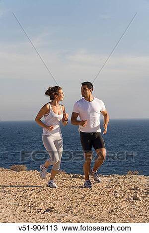 Stock Image - Couple jogging in a cliff by the sea in Ibiza. Fotosearch