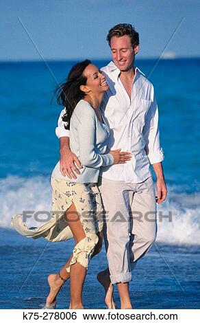 couple laughing as they walk along the beach View Large Photo Image Stock Photograph - couple laughing as they walk along the beach. Fotosearch