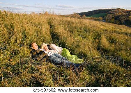 Stock Image - Couple lying in field in the sunshine. Fotosearch