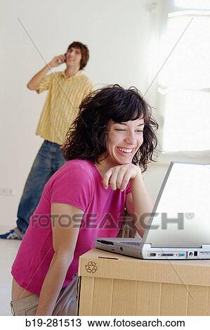 Stock Image - Couple moving home, the girl with laptop while the boy with mobile phone. Fotosearch