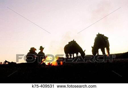 Stock Image - Couple of ranchers at campfire with horses. Fotosearch