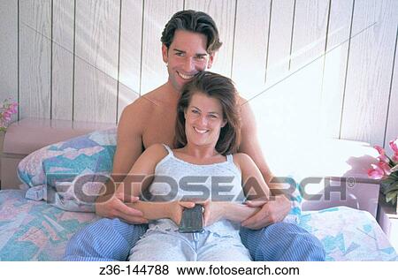 Stock Photo - Couple on bed watching TV. Fotosearch