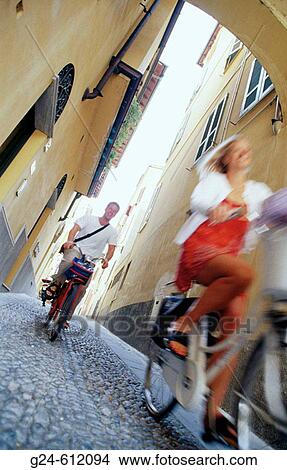 Picture - Couple on bikes in a street of Cremona. Italy. Fotosearch