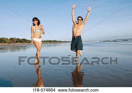 Picture - couple playing and jumping on beach. Fotosearch