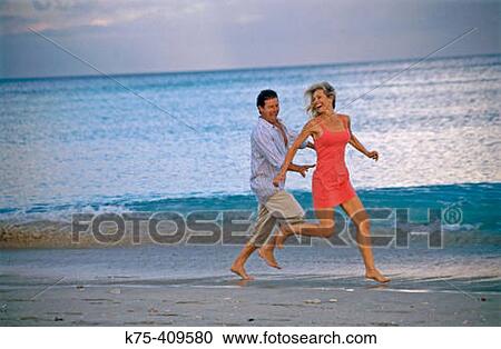Stock Image - Couple running along beach. Fotosearch