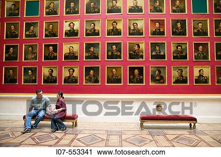 Stock Image - Couple seated in front of portrait gallery of the portrait gallery of the 1812 war heroes in the Hermitage Museum (Winter Palace). St Petersburg. Russia. Fotosearch