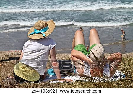 Stock Image - Couple sitting at Salinas beach, Asturias, Spain. Fotosearch
