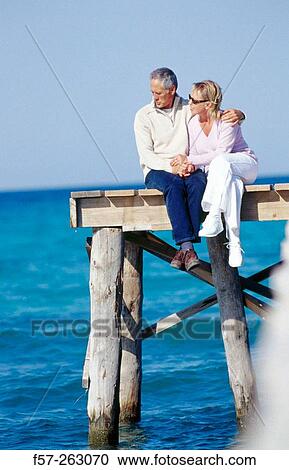 Couple sitting down in a wooden footbridge over the sea View Large Photo Image Stock Image - Couple sitting down in a wooden footbridge over the sea. Fotosearch