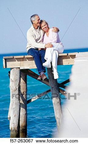 Couple sitting down in a wooden footbridge over the sea View Large Photo Image Stock Photo - Couple sitting down in a wooden footbridge over the sea. Fotosearch