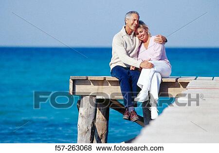 Couple sitting down in a wooden footbridge over the sea View Large Photo Image Stock Photo - Couple sitting down in a wooden footbridge over the sea. Fotosearch