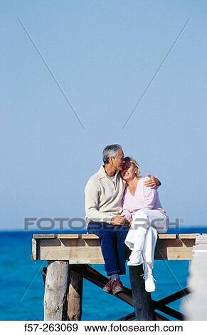 Couple sitting down in a wooden footbridge over the sea View Large Photo Image Stock Photo - Couple sitting down in a wooden footbridge over the sea. Fotosearch