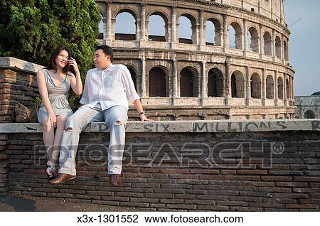 Stock Image - Couple sitting in front of the Roman Colosseum. Fotosearch