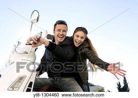 Stock Image - Couple sitting on a motor scooter and cheering. Fotosearch