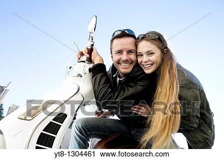Couple sitting on a motor scooter and smiling View Large Photo Image Stock Image - Couple sitting on a motor scooter and smiling. Fotosearch