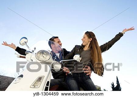 Stock Photo - Couple sitting on a motor scooter and raising their arms in the air. Fotosearch