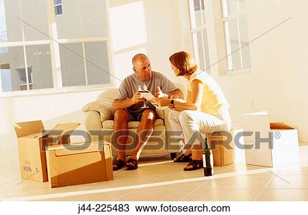 Stock Image - Couple sitting on chair and boxes looking at paint chart in their new house. Fotosearch