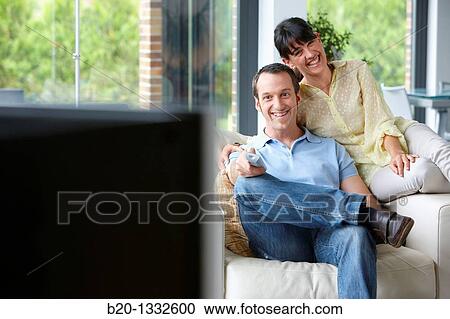 Couple sitting on coach watching TV in the living room View Large Photo Image Stock Image - Couple sitting on coach watching TV in the living room. Fotosearch
