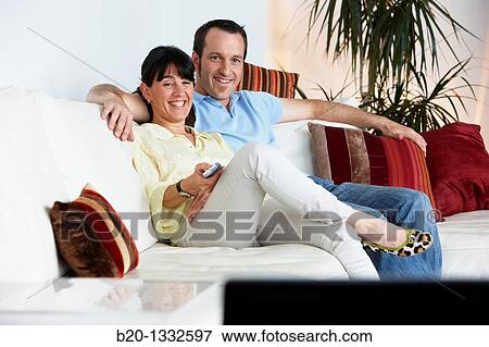 Couple sitting on coach watching TV in the living room View Large Photo Image Stock Photo - Couple sitting on coach watching TV in the living room. Fotosearch