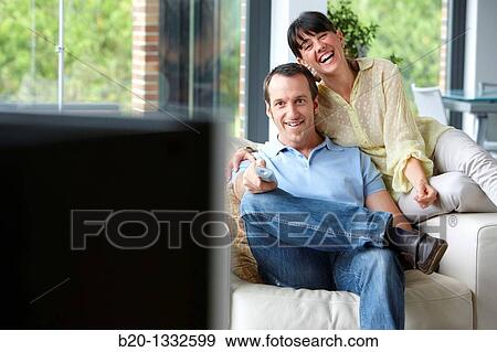 Couple sitting on coach watching TV in the living room View Large Photo Image Stock Photo - Couple sitting on coach watching TV in the living room. Fotosearch