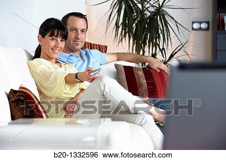 Couple sitting on coach watching TV in the living room View Large Photo Image Stock Photograph - Couple sitting on coach watching TV in the living room. Fotosearch