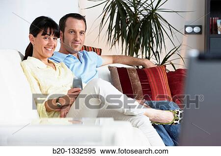 Couple sitting on coach watching TV in the living room View Large Photo Image Stock Photography - Couple sitting on coach watching TV in the living room. Fotosearch