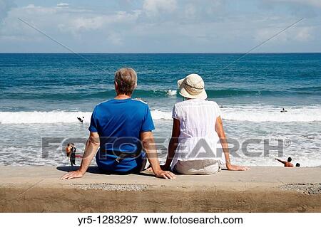 Couple sitting on sea wall watching surfers at La Cicer, Playa de Las Canteras, Las Palmas, Gran Canaria, Canary Islands, Spain View Large Photo Image Stock Photo - Couple sitting on sea wall watching surfers at La Cicer, Playa de Las Canteras, Las Palmas, Gran Canaria, Canary Islands, Spain. Fotosearch
