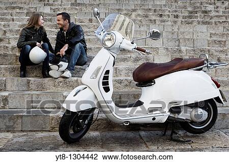 Stock Image - Couple sitting on steps next to motor scooter. Fotosearch