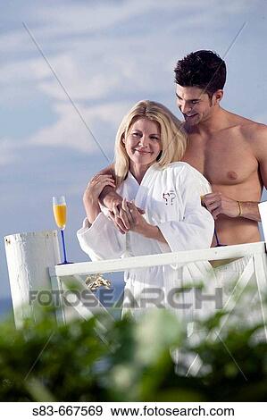 Stock Photo - Couple standing on deck in robes at beach. Fotosearch
