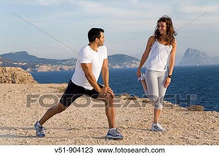 Stock Image - Couple stretching by the sea in a cliff in Ibiza. Fotosearch