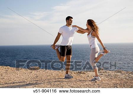 Stock Photograph - Couple stretching by the sea in a cliff in Ibiza. Fotosearch