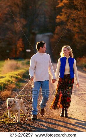 Couple strolling a country road with their dog View Large Photo Image Stock Photo - Couple strolling a country road with their dog. Fotosearch