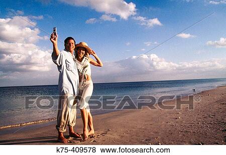 Couple taking photos of themselves on beach with camera phone View Large Photo Image Stock Photo - Couple taking photos of themselves on beach with camera phone. Fotosearch