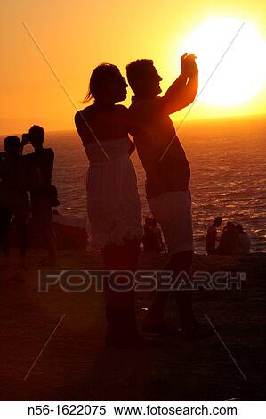 COUPLE TAKING PICTURES DURING THE SUNSET, MIKONOS, GREECE View Large Photo Image Stock Photography - COUPLE TAKING PICTURES DURING THE SUNSET, MIKONOS, GREECE. Fotosearch