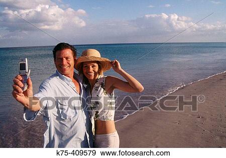 Couple using camera phone at the beach View Large Photo Image Stock Photo - Couple using camera phone at the beach. Fotosearch