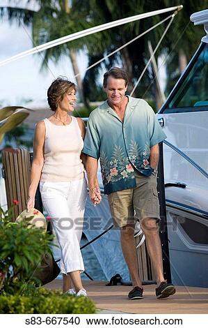 Couple walking down dock with boats in the background View Large Photo Image Stock Image - Couple walking down dock with boats in the background. Fotosearch