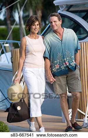 Couple walking down dock with boats in the background View Large Photo Image Stock Image - Couple walking down dock with boats in the background. Fotosearch
