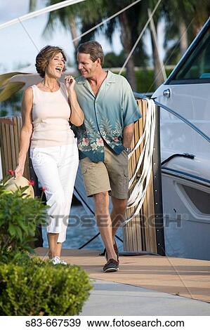Couple walking down dock with boats in the background View Large Photo Image Stock Photo - Couple walking down dock with boats in the background. Fotosearch