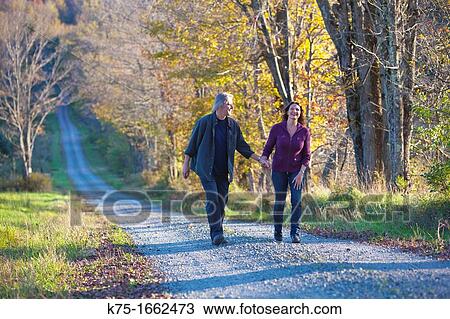 Couple walking holding hands on country road View Large Photo Image Stock Image - Couple walking holding hands on country road. Fotosearch