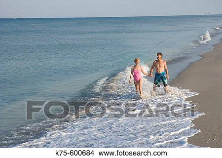 Picture - Couple walking through surf. Fotosearch