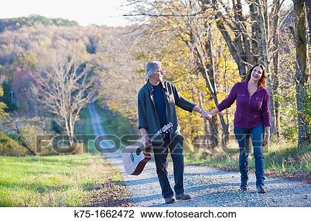 Stock Image - Couple walking with guitar on country road. Fotosearch