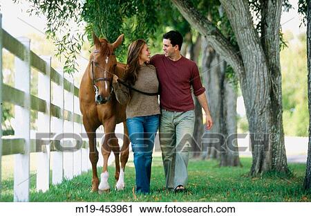 Stock Image - couple walking with their horse. Fotosearch