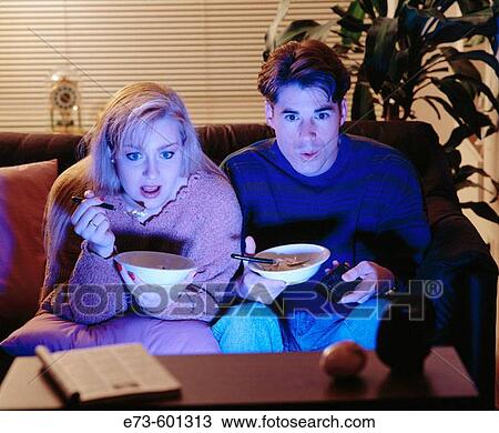 Stock Image - Couple watching intense movie, eating ice cream. Fotosearch