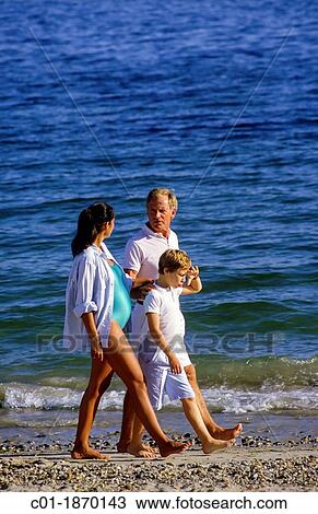 Stock Image - Couple with pregnant woman and boy strolling on beach. Fotosearch
