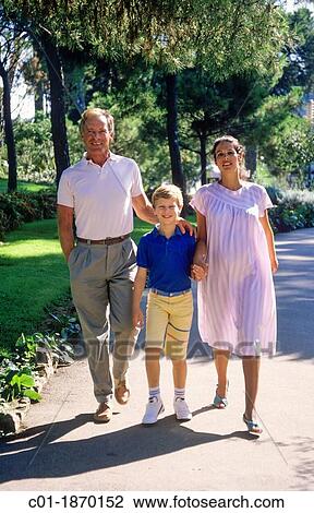 Stock Image - Couple with pregnant woman and boy strolling in park. Fotosearch