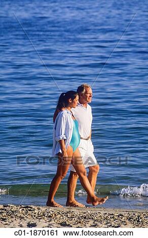 Stock Image - Couple with pregnant woman strolling on beach. Fotosearch