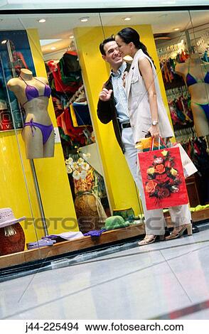 Couple with shopping bags by display window in shopping mall View Large Photo Image Picture - Couple with shopping bags by display window in shopping mall. Fotosearch