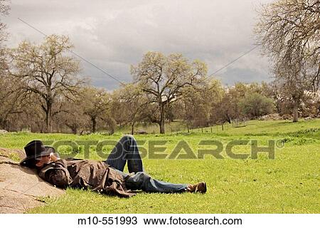Cowboy in western attire laying down up against a rock during the break of a storm in a beautiful countryside landscape View Large Photo Image Stock Image - Cowboy in western attire laying down up against a rock during the break of a storm in a beautiful countryside landscape. Fotosearch