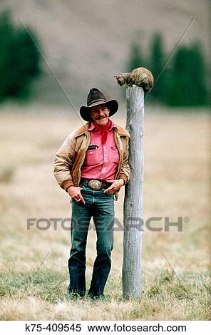Stock Photography - Cowboy standing next to cat on pole. Fotosearch